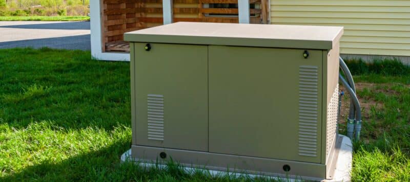 Standby generator unit installed outside a home, with ventilation grates and connected cables